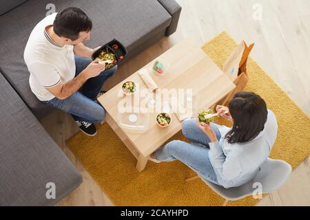 Au-dessus de la vue portrait de l'homme et de la femme mangeant un déjeuner à emporter au bureau ou à la maison tout en étant assis sur un grand canapé, espace de copie Banque D'Images