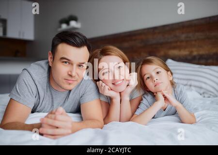 portrait de belle famille heureuse couché sur le lit ensemble, mère père et fille de kid embrassant embrassant et rire. à l'intérieur Banque D'Images