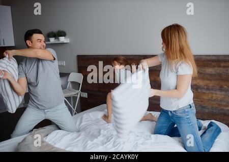 la famille de caucasiens heureux se composait de mère père et fille d'enfant s'amuser ensemble jouant avec des oreillers à la maison sur le lit Banque D'Images