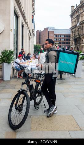 Jeune homme avec vélo en attente d'une commande de nourriture deliveroo Dans un bistro de Castle Street à Liverpool Banque D'Images