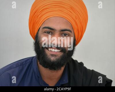 Un jeune Indien charmant, le dévot de Sikh, avec une barbe noire et des yeux souriants, porte un turban orange (dastar) et regarde dans l'appareil photo. Banque D'Images