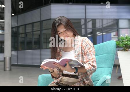 Femme asiatique assise sur une chaise et lisant un livre Banque D'Images