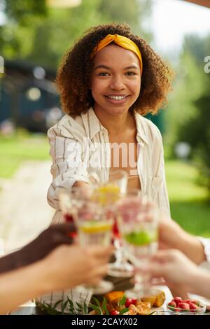 Portrait vertical d'une jeune femme souriante en train de griller avec des amis tout en appréciant le dîner sur la terrasse extérieure en été Banque D'Images
