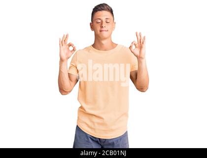 Jeune homme beau portant des vêtements décontractés et souriant avec les yeux fermés faisant un geste de méditation avec les doigts. Concept de yoga. Banque D'Images