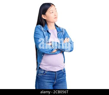 Jeune belle femme chinoise enceinte s'attendant à un bébé regardant à côté avec les bras croisés convaincu et confiant Banque D'Images