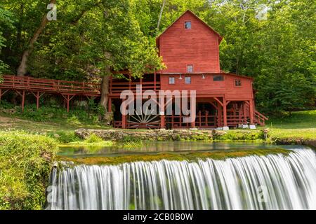 Un vieux moulin à grate rouge avec une petite cascade. Banque D'Images