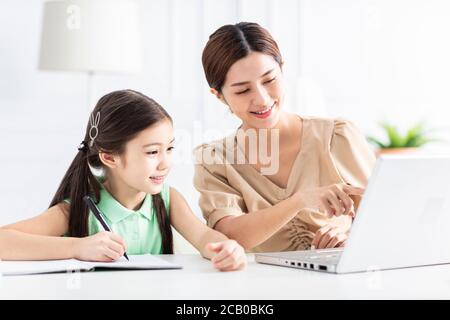 Mère avec fille regardant l'ordinateur portable et travaillant à la maison Banque D'Images