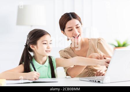 Mère avec fille regardant l'ordinateur portable et travaillant à la maison Banque D'Images