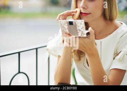 Image rognée d'une jeune femme regardant un miroir compact et application de poudre pour le visage Banque D'Images