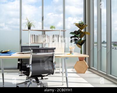 Intérieur de bureau moderne avec grandes fenêtres avec vue sur le ciel bleu. Bureau en bois dans le coin d'un lieu de travail contemporain. Deux chaises vides avec ordinateur portable Banque D'Images