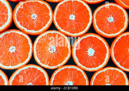 Les oranges rouges ou les pamplemousses sont coupées en deux sur fond noir. Banque D'Images