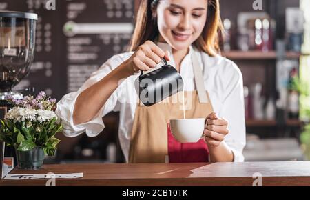 Le Barista asiatique verse du lait dans une tasse de café, c'est-à-dire un espresso au latte ou un cappuccino pour une commande client dans un café, un propriétaire de petite entreprise et un restaurant Banque D'Images