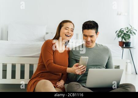 Couple asiatique joyeux assis avec un ordinateur et un smartphone pour passer un appel vidéo. Concept de connexion en ligne et de technologie sans fil Banque D'Images