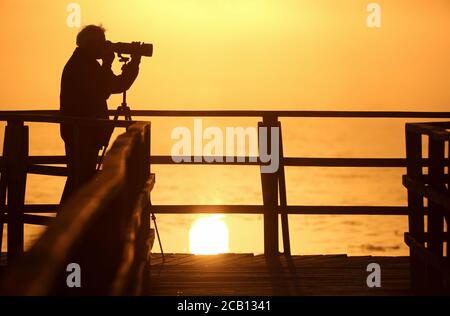 Bad Buchau, Allemagne. 10 août 2020. Un homme se tient sur la jetée de Federsee peu après le lever du soleil et prend des photos pendant que le soleil se reflète dans le lac. Credit: Thomas Warnack/dpa/Alay Live News Banque D'Images