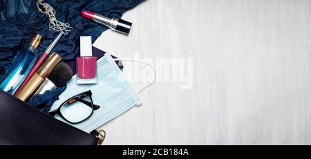 Masque chirurgical avec divers produits cosmétiques et de maquillage tombant dans un sac femelle, poser à plat avec copie espace Banque D'Images