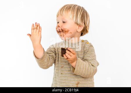 Adorable tout-petit blond mangeant une barre de chocolat avec grand plaisir, fond blanc, Pologne Banque D'Images