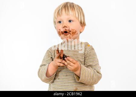 Adorable tout-petit blond mangeant une barre de chocolat avec grand plaisir, fond blanc, Pologne Banque D'Images