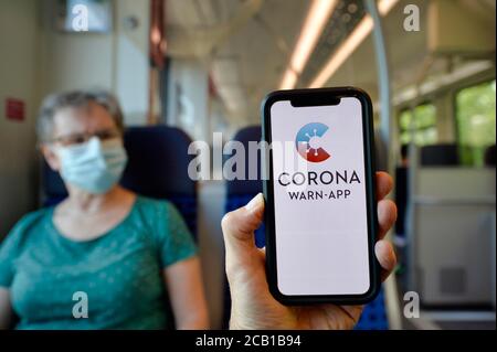 Mains tient un smartphone avec application d'avertissement de corona devant une femme âgée avec masque de visage assis à S-Bahn, train, crise de corona, Stuttgart Banque D'Images