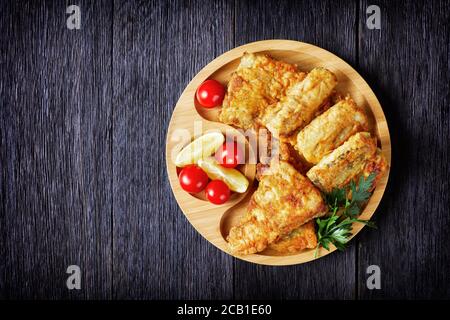 Filet de merlu poêlé servi sur une assiette de bambou écologique avec des quartiers de citron, des tomates cerises sur fond de bois foncé, gros plan, copie sp Banque D'Images