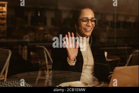 Femme d'affaires ayant un appel vidéo sur son ordinateur portable. Femme professionnelle assise dans un café avec des écouteurs et se portant sur un ordinateur portable. Banque D'Images