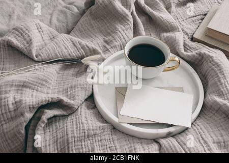 Petit-déjeuner dans le décor de maquette de papeterie de lit. Tasse de café, carte de vœux vierge, enveloppe sur plateau en marbre blanc. Sécher le feuillage herbacé de Lagurus ovatus Banque D'Images