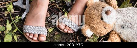 Récolte panoramique de pieds de gamin afro-américain près de sale ours en peluche au sol dans une rue urbaine Banque D'Images
