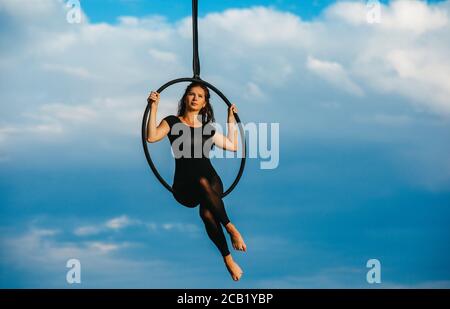 Une femme aerialiste interprète des éléments acrobatiques dans un panier suspendu sur fond de ciel bleu et de nuages blancs. Banque D'Images