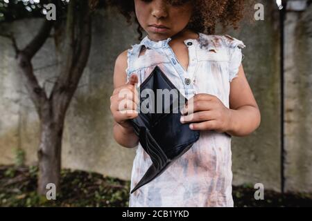 Vue rognée d'un enfant afro-américain pauvre portant un portefeuille vide sur la rue urbaine Banque D'Images