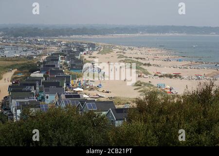 Les gens apprécient le temps chaud en bord de plage huttes sur Mudeford Sandbank, Dorset. Banque D'Images