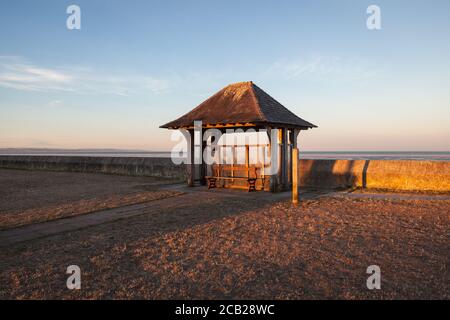 Le soleil se trouve sur un abri et un banc traditionnels en bord de mer. Banque D'Images