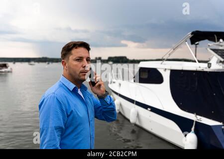 Homme parlant au téléphone à côté du yacht de luxe au port. Concept marin et marin Banque D'Images