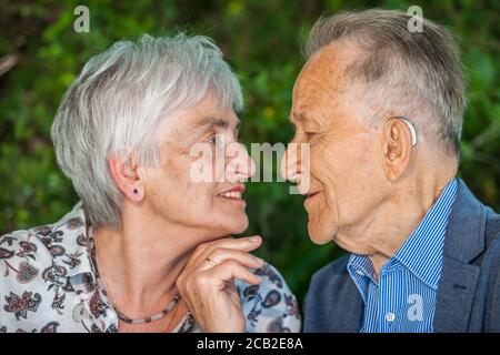 Vue de la tête et de l'épaule d'un couple retraité âgé devant un arrière-plan vert flou juste avant un baiser. Banque D'Images