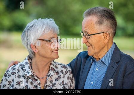 Portrait tête-et-épaule d'un couple aîné qui regarde avec amour avec des lunettes devant l'arrière-plan flou d'un parc. Banque D'Images