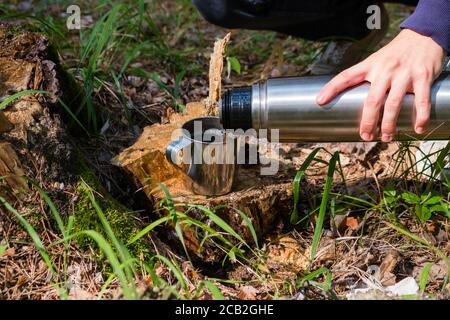 le randonneur verse le thé d'un thermos dans une forêt d'été Banque D'Images