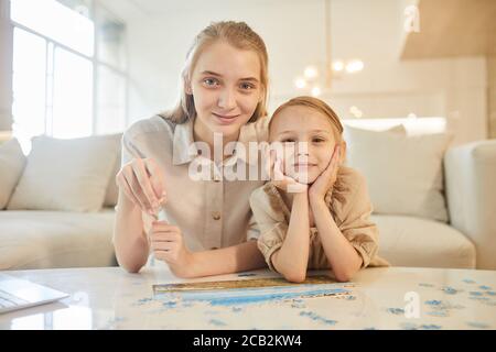 Portrait aux tons chauds de deux sœurs qui se réunissent pour résoudre des énigmes tout en appréciant le temps à l'intérieur à la maison et en regardant l'appareil photo, l'espace de copie Banque D'Images