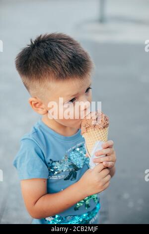 Bébé garçon enfant qui mange de la glace au chocolat dans le cône de gaufres. Banque D'Images