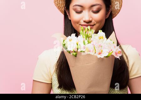 fille asiatique positive en chapeau de paille odeur de fleurs isolées dessus rose Banque D'Images