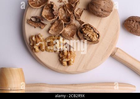 Photo grand angle de noix sur une planche en bois avec un marteau en bois sur une surface blanche Banque D'Images
