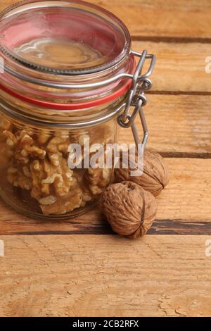 Gros plan vertical de noix décortiquées dans un pot en verre et noix entières sur une table en bois Banque D'Images