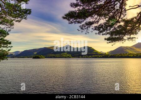 Surface ensoleillée du lac Derwentwater avec une chaîne de montagnes verdeuses derrière vu à travers les branches d'arbre Banque D'Images