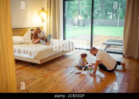Mère et fille assise sur le lit, maman embrassant l'enfant. Père avec son fils jouant sur le sol. Concept de famille Banque D'Images