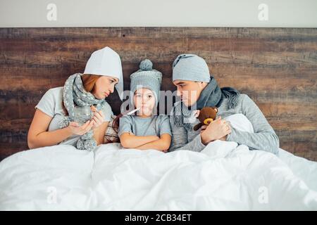 portrait d'une fillette malade qui a de la fièvre, qui souffre du tabac à priser, des parents allongé sur le lit avec elle et de soutien, traitant, portant des chapeaux et des foulards Banque D'Images