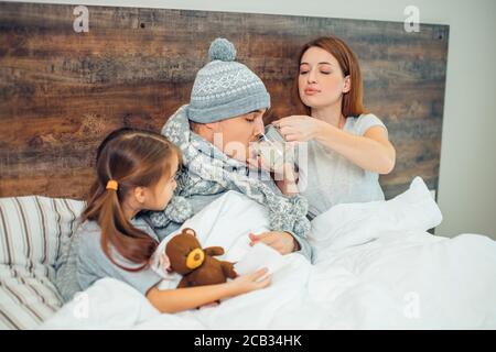 femme caucasienne soigneuse donner des médicaments au mari, traitement réussi par la femme. enfant fille assis avec des parents et le soutien Banque D'Images