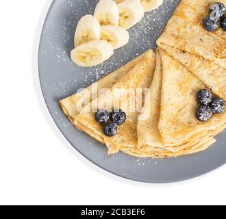 Vue de dessus d'un dessert sur une assiette de gris recouverte de fruits. Crêpes fines avec myrtille et banane isolées sur blanc Banque D'Images