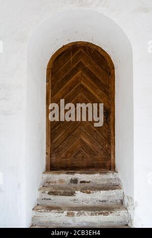 Très ancienne porte en bois arrondie et porte de l'âge médiéval. Entrée dans le bâtiment blanc. Style rustique. Banque D'Images