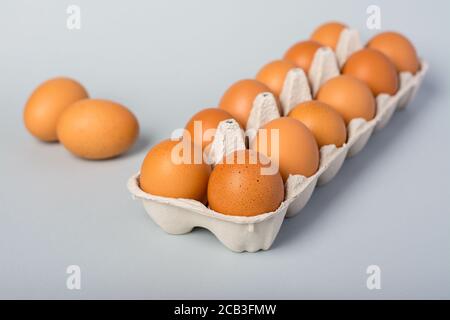 Oeufs de poulet crus dans une boîte à oeufs et deux oeufs à côté sur fond gris Banque D'Images