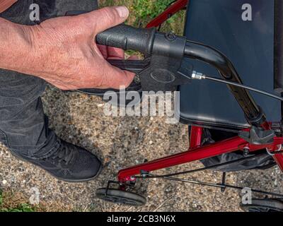 Gros plan POV d'un homme âgé debout avec sa main droite tenant la poignée droite et le frein d'une poussette/roller adulte. Banque D'Images