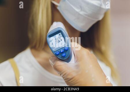 La main du médecin dans un gant de protection contient un thermomètre infrarouge et mesure la température du patient. Mesure à distance de la forte fièvre pour Banque D'Images