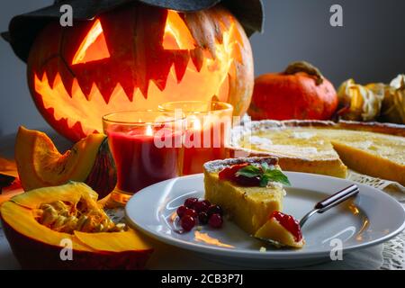 Petit gâteau de citrouille maison d'halloween avec feuille de menthe et confiture de baies de vache sur une assiette blanche. Bougies et Jack-o-lanterne en chapeau sur fond. Cuisine traditionnelle de vacances Banque D'Images