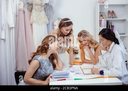 sympathique, belle apparence tailleur s'asseoir avec des modèles sur la table au bureau, jeunes filles dans des robes de mariage faites par le designer professionnel, elle les consulta et Banque D'Images